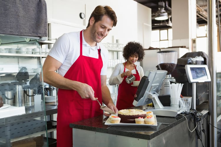 Smiling waiter slicing cake with waitress behind him at the bakery. Learn how to measure the ROI of training and development in restaurants.