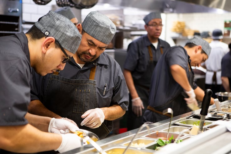 Restaurant workers looking through ingredients on the make-line. Learn more about digitizing inventory processes and measuring the return on investment ROI of restaurant inventory software.